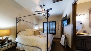 Een slaapkamer met een hemelbed, een plafondventilator, een aan de muur bevestigde televisie en een houten dressoir.