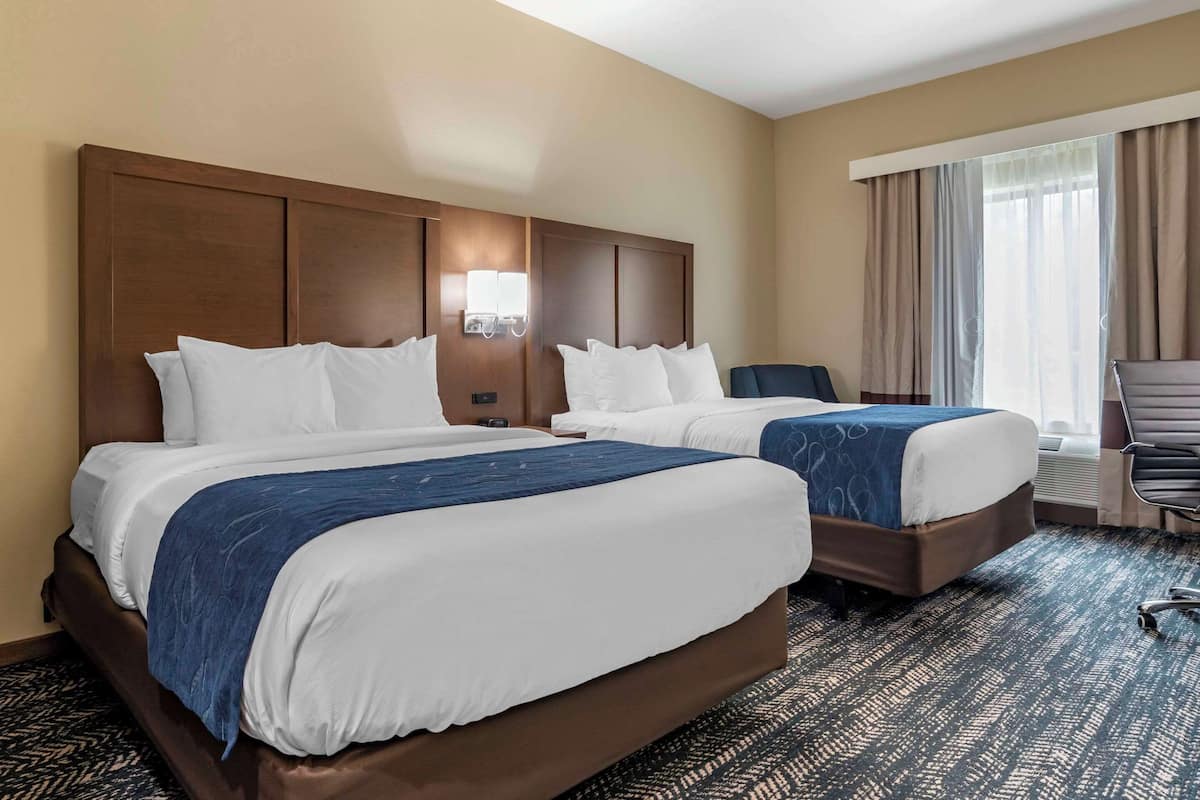 A hotel room with two beds, a large wooden headboard, a desk, and a chair.