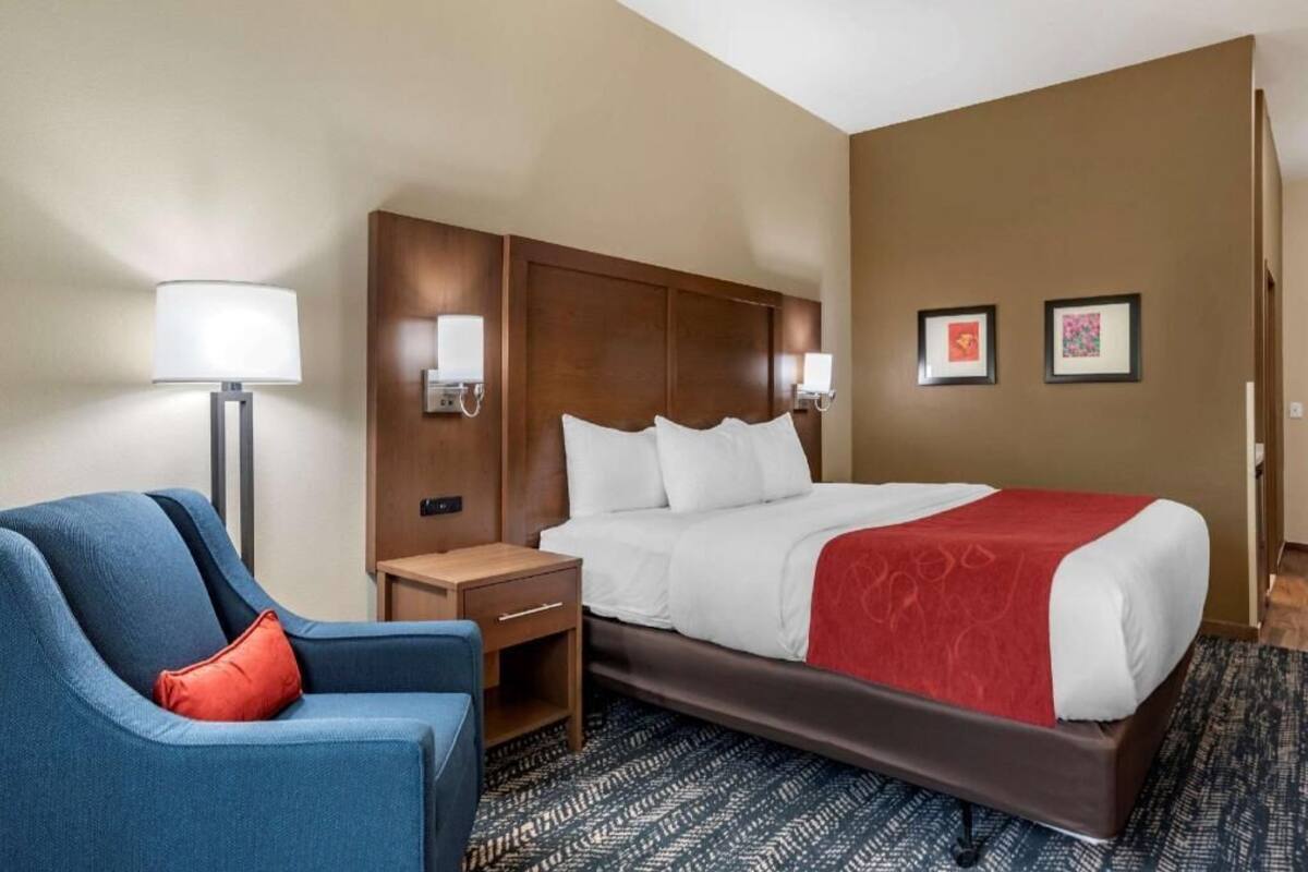 A hotel room with a bed, a blue armchair, a nightstand, a lamp, and two framed pictures on the wall.