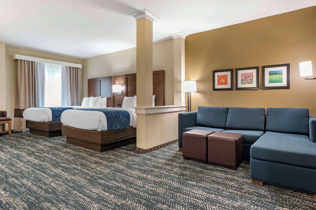 A hotel room with two beds, a sofa, a desk, and a chair.
