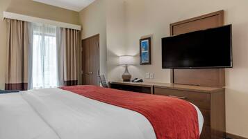 A hotel room with a large bed, a desk with a lamp, a flat-screen TV, and a door.