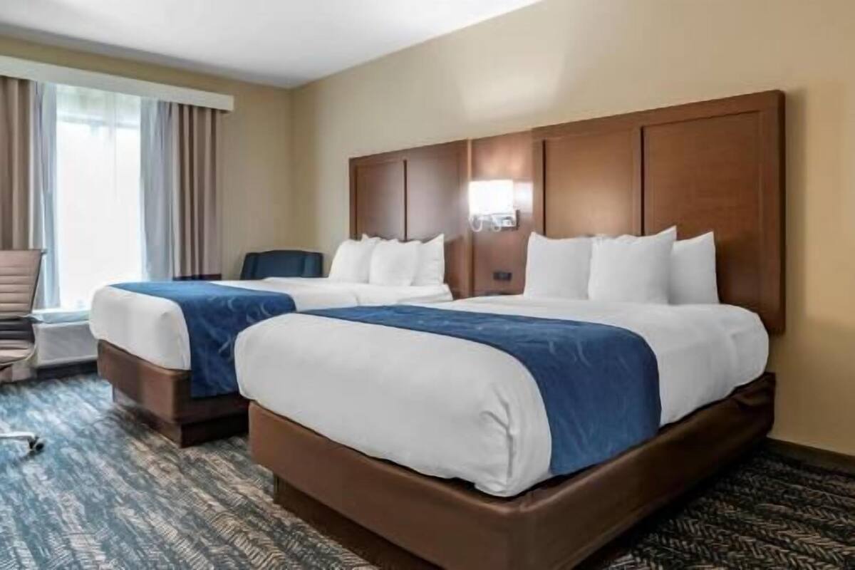 A hotel room with two beds, a desk, and a chair.
