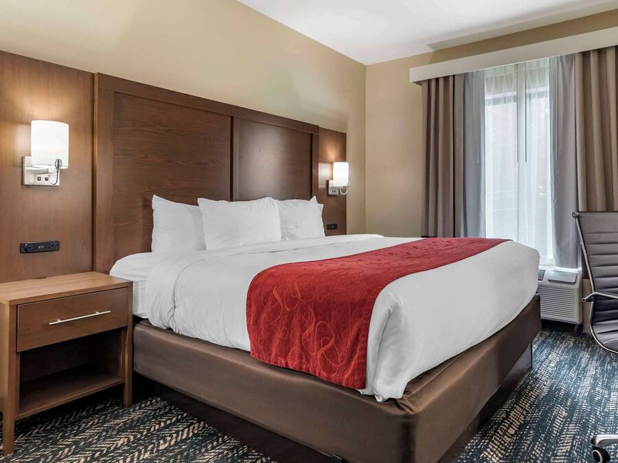 A hotel room with a large bed, two bedside tables, a chair, and a window with curtains.