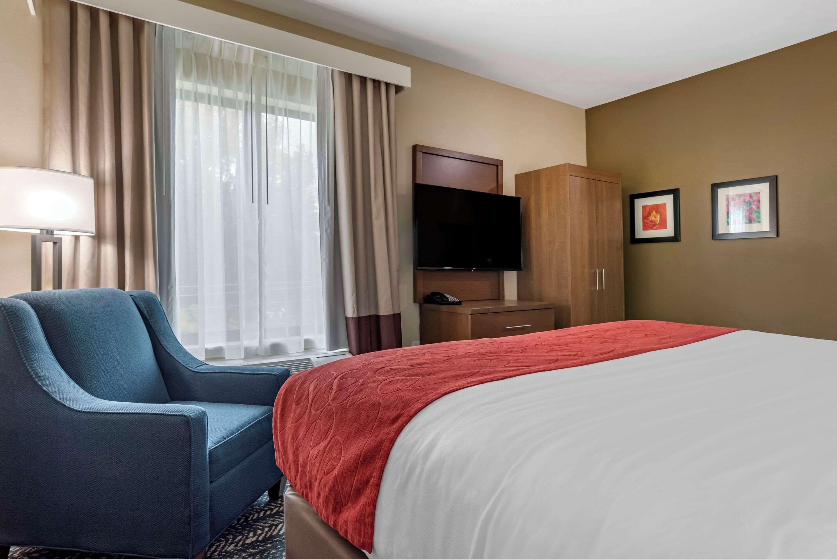 Una habitación de hotel con cama, una silla, un televisor, un armario y cortinas.