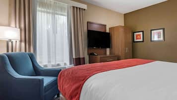 Una habitación de hotel con cama, una silla, un televisor, un armario y cortinas.
