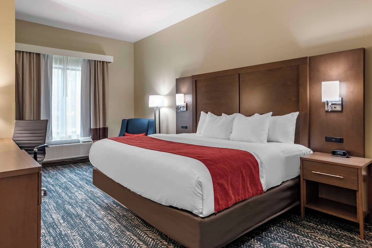 A hotel room with a large bed, a desk, a chair, and a window with curtains.