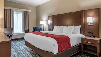 Ein Hotelzimmer mit einem großen Bett, einem Schreibtisch, einem Stuhl und einem Fenster mit Vorhängen.