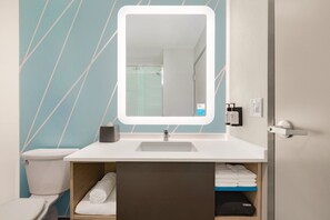 Un baño con lavamanos blanco, un espejo con luz, inodoro y un perchero para toallas.