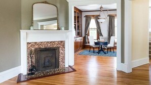 A spacious living room with a brick fireplace, wooden flooring, and a dining area with a chandelier. - EAA Historical Home in the heart of Oshkosh  (Oshkosh)