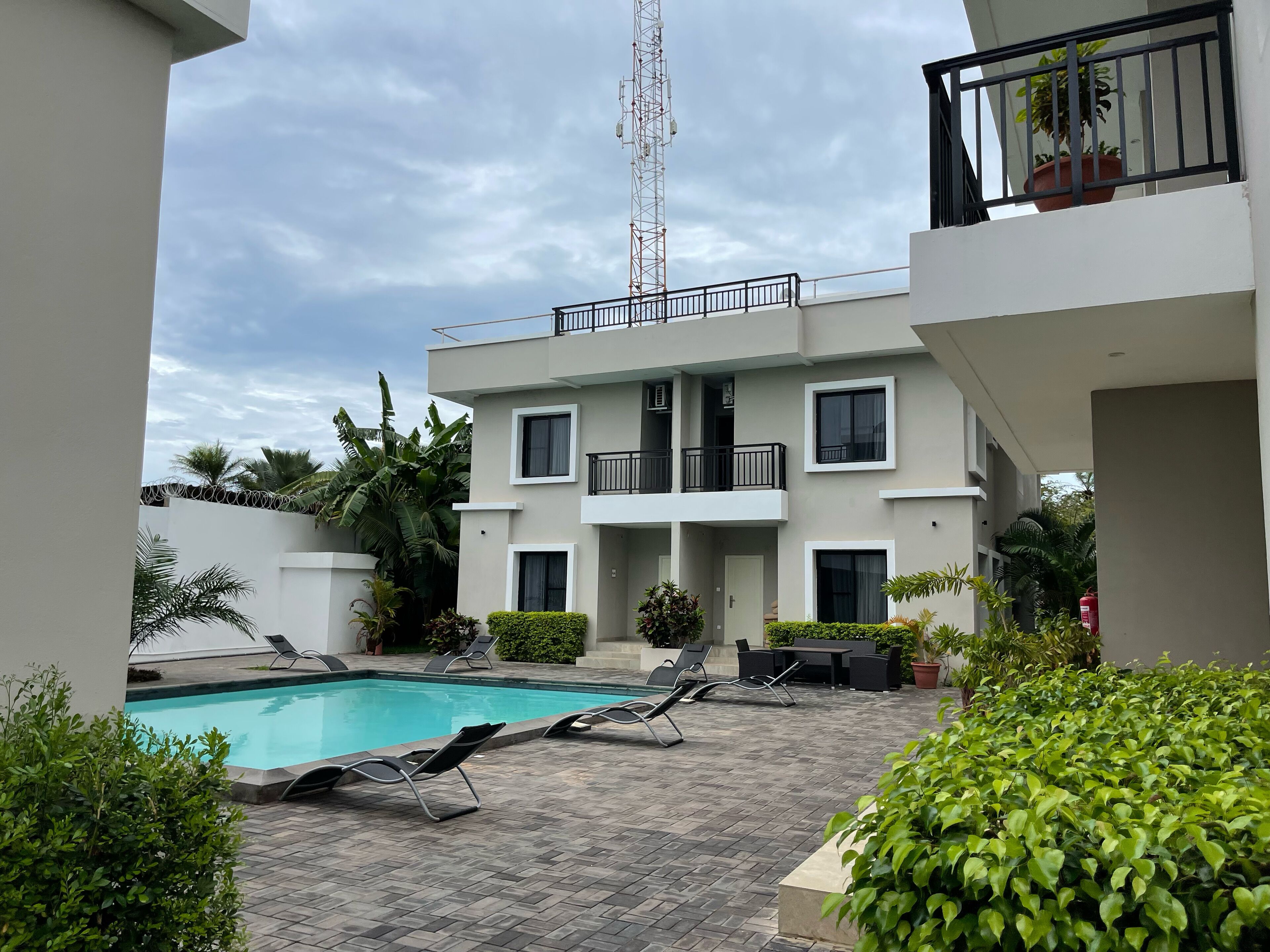 A modern building with a swimming pool, lounge chairs, and potted plants.