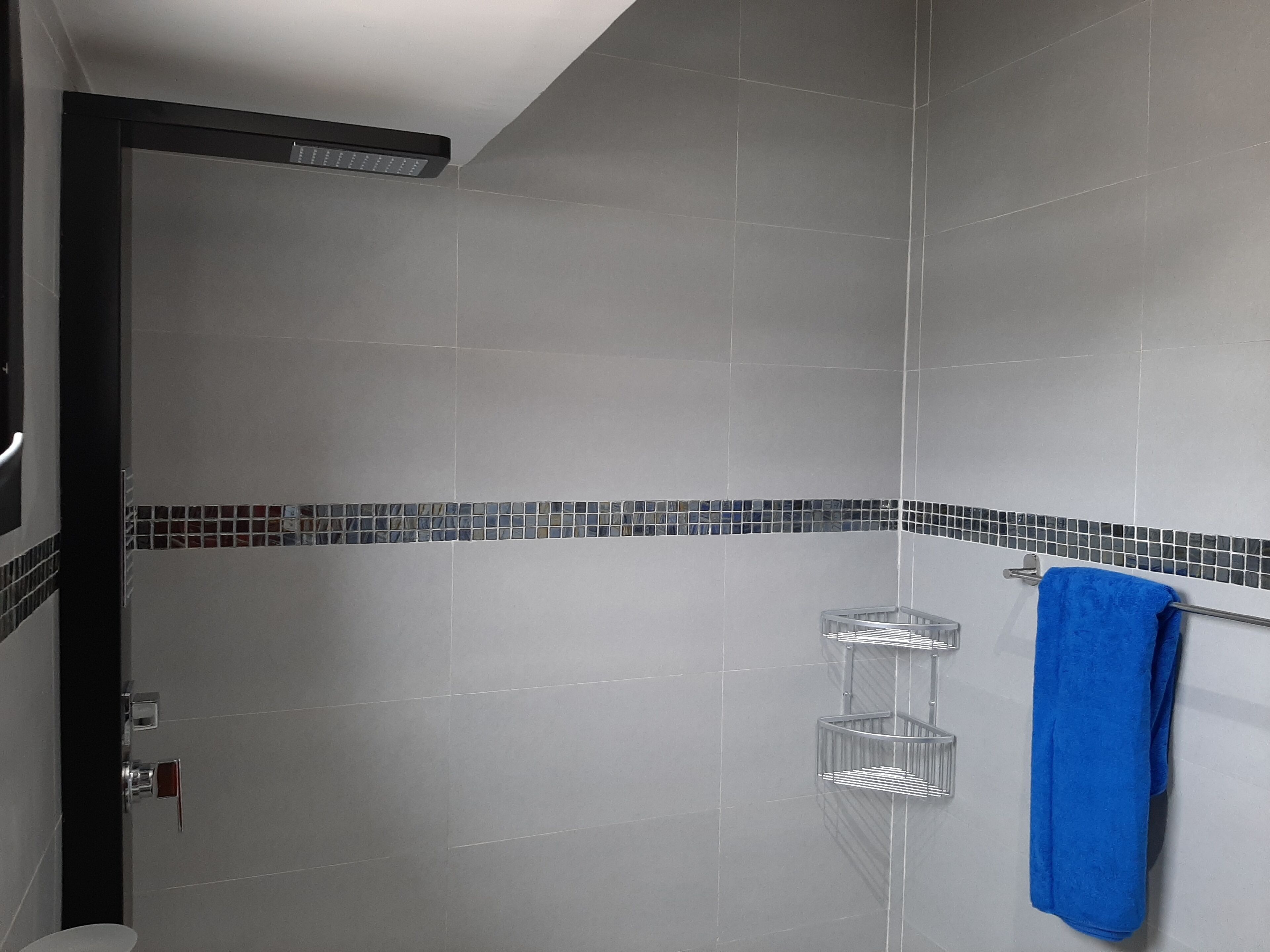 Un espace douche avec des carreaux gris, une serviette bleue posée sur un porte-serviettes et une petite étagère.