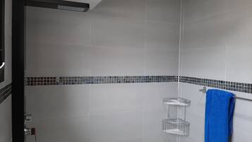 Un espace douche avec des carreaux gris, une serviette bleue posée sur un porte-serviettes et une petite étagère.