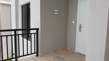 Um corredor com uma porta branca, uma placa com letras e um corrimão preto.