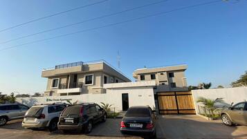A modern building with a flat roof and a gated entrance. There are several parked cars in front.