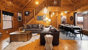 A log cabin interior with a wooden staircase, a dining area, and a living room with a leather sofa.