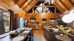 A wooden cabin interior with a dining area, kitchen, and living space.