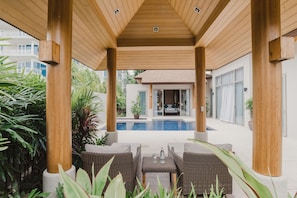 A covered outdoor seating area with wicker furniture, a pool, and a view of a building with large windows.