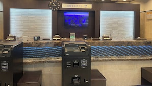 A hotel reception area with a clock, a television displaying a cityscape, and a self-service kiosk.