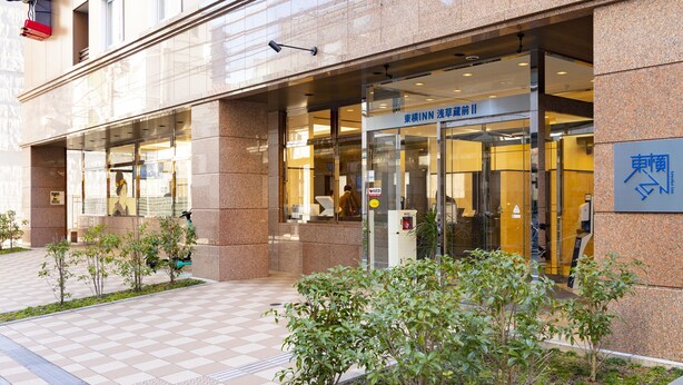 A modern building with a glass entrance, a sign reading "東横INN 浅草前", and a wheelchair-accessible ramp.