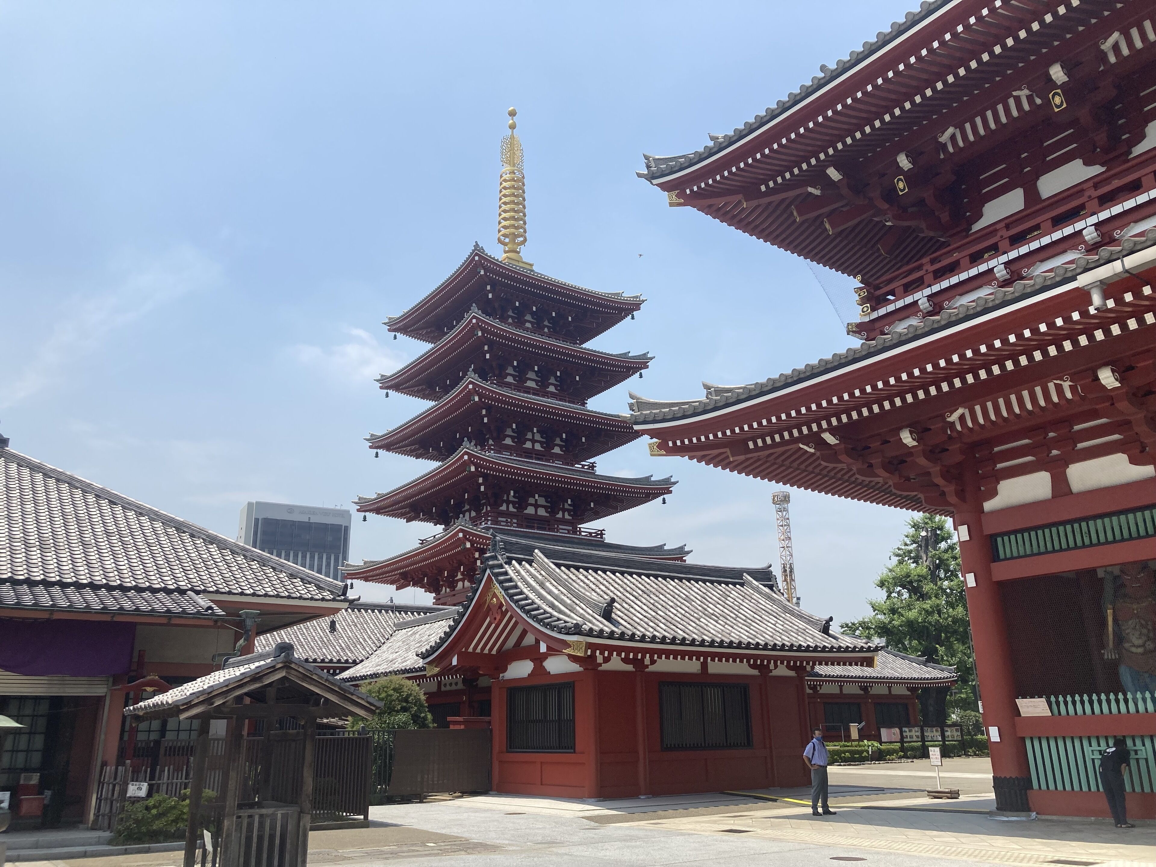 A traditional multi-tiered pagoda with a golden spire, surrounded by red and white buildings with tiled roofs.