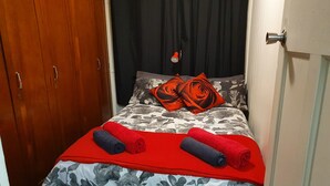 Een net opgemaakt bed met bloemenbeddels, een rode deken en twee opgerolde handdoeken.