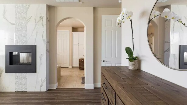 A hallway with a wooden floor, a black-framed picture, a white orchid, and a mirror on the wall.