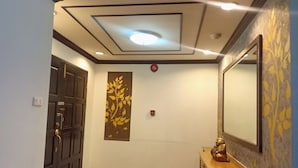 A hallway with a wooden door, a wall-mounted decorative panel, a ceiling light, and a wooden console with a statue. - Supha Maison (Bangkok)