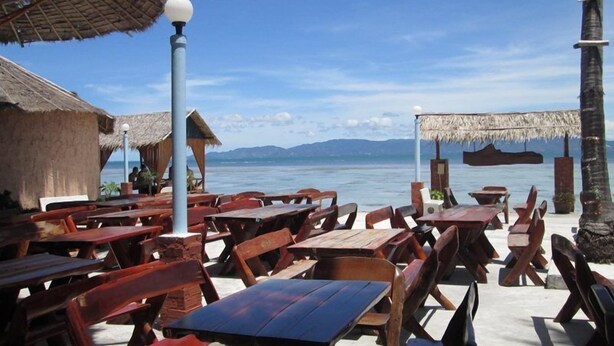 A beachside restaurant with wooden tables and chairs, thatched-roof huts, and a view of the sea. - Power Beach Resort (Ko Pha-ngan)