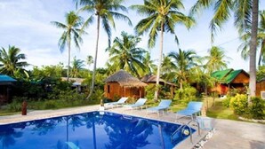 A swimming pool surrounded by palm trees and thatched-roof huts. - Power Beach Resort (Ko Pha-ngan)