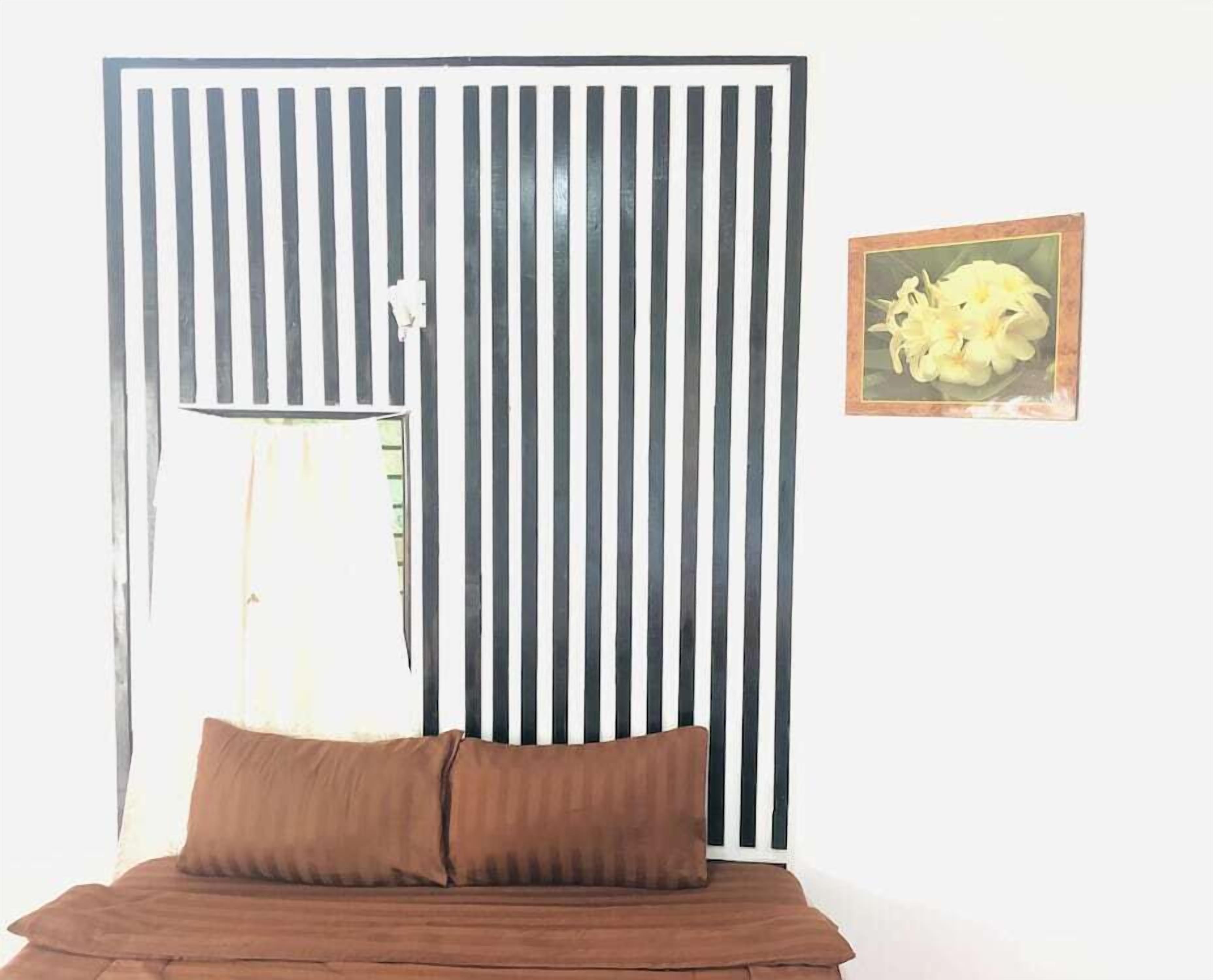 A room with a bed, a striped partition, a framed picture, and a lamp.