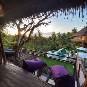 A wooden deck with purple cushions, overlooking a pool and lush greenery. - Room on the Real Tree (Bali)