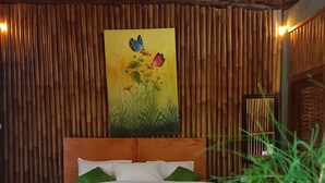 A bed with white bedding, green pillows, and a wooden headboard. A painting of butterflies and flowers hangs above the bed. - Room on the Real Tree (Bali)