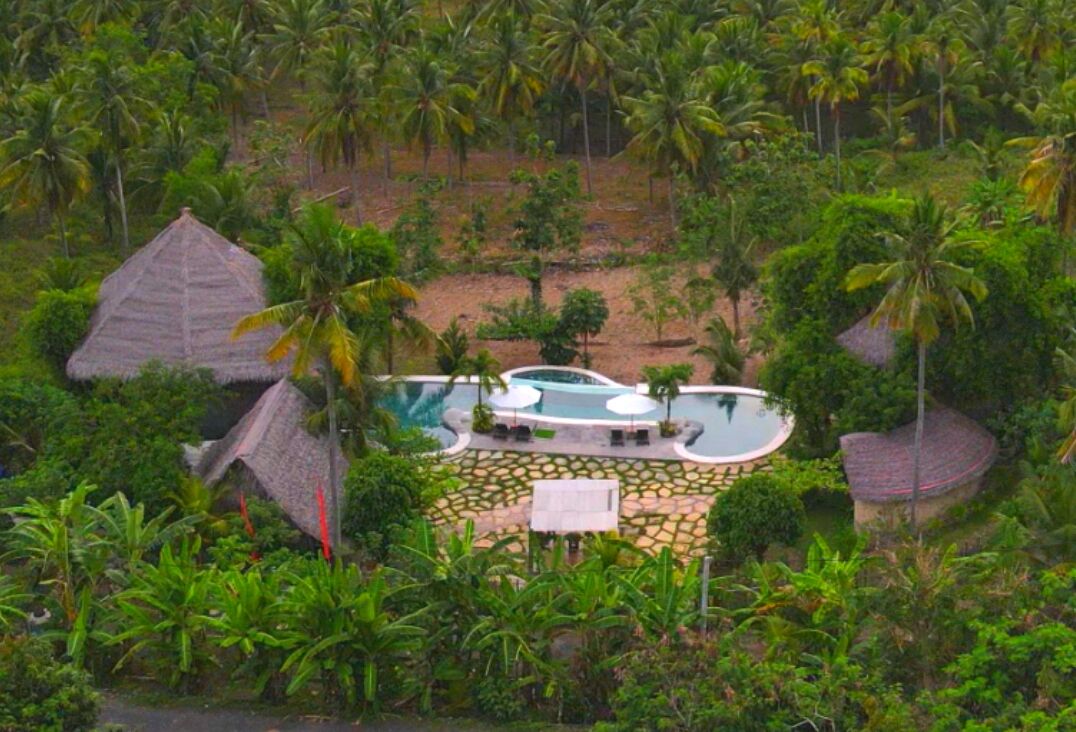 Et resort med pool omgivet af palmer og parasolhytter.