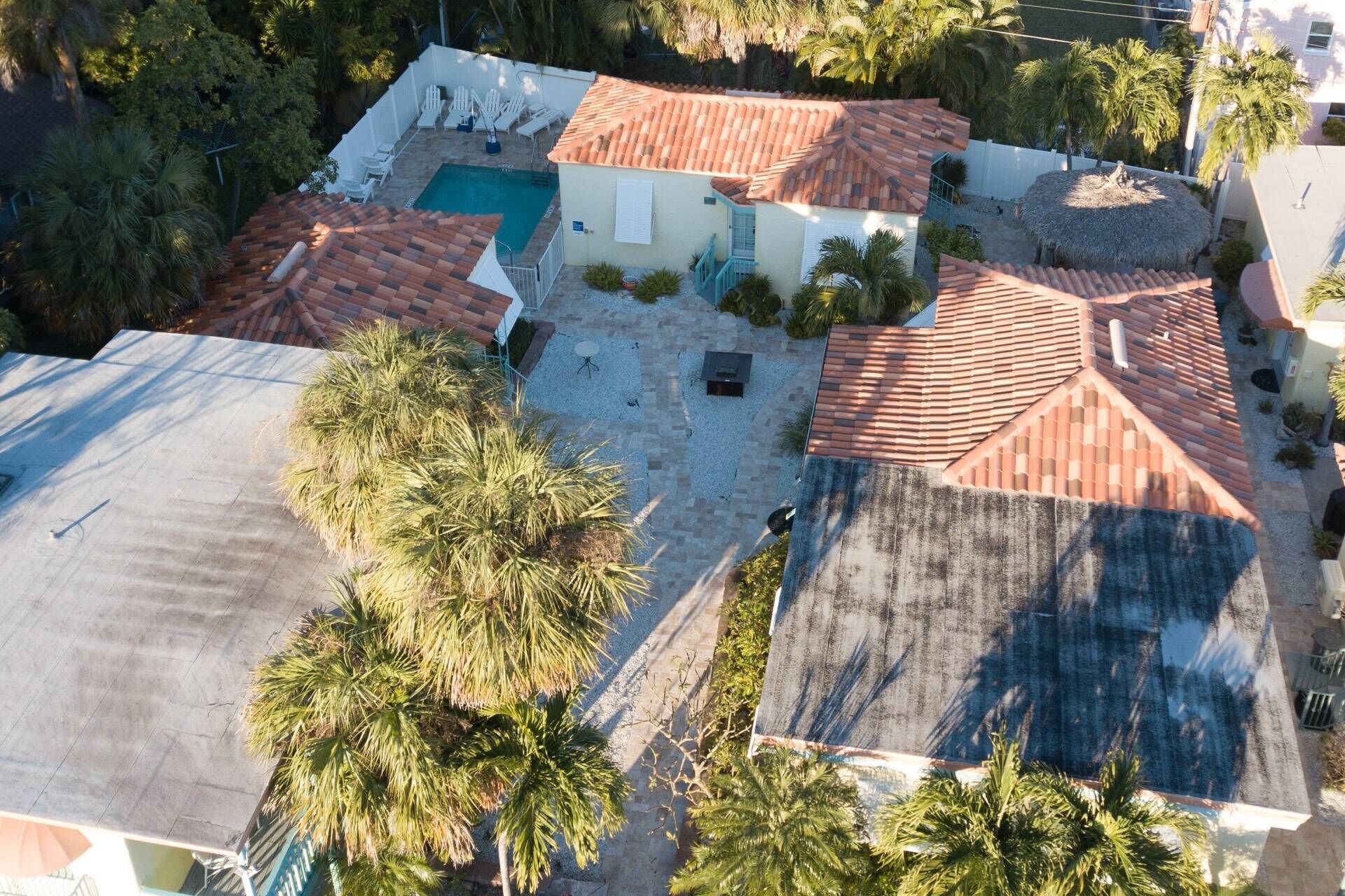 Una propiedad residencial con piscina, varios techos de tejas rojas y palmeras.