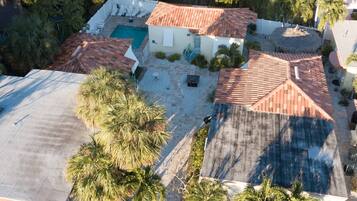 Una propiedad residencial con piscina, varios techos de tejas rojas y palmeras.