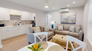 A modern living space with a kitchen, a sofa set, a dining table, and a ceiling fan.