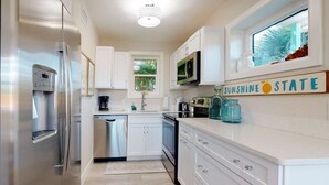 A modern kitchen with stainless steel appliances, white cabinetry, and a window with a view of greenery.
