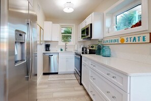 A modern kitchen with stainless steel appliances, white cabinetry, and a window with a view of greenery.
