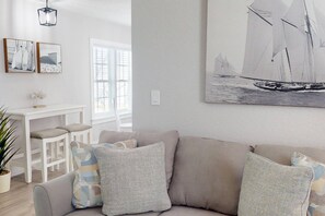 A living room with a sofa, a dining table with chairs, a potted plant, and a large sailboat painting on the wall.