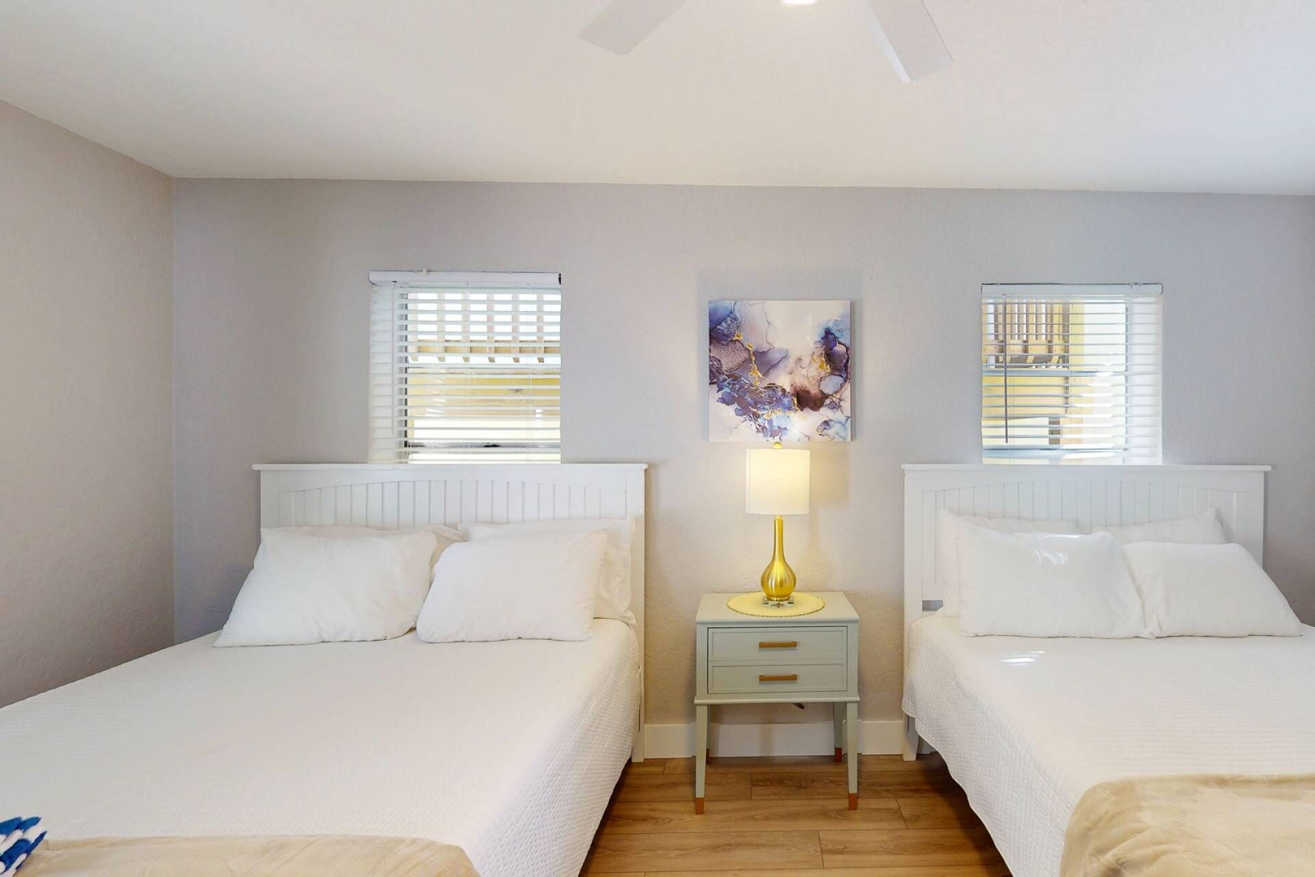A bedroom with two beds, a nightstand with a lamp, and a painting on the wall.