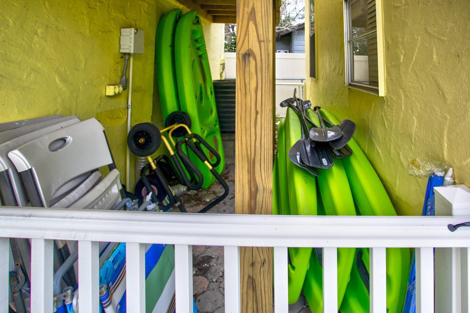 Een smalle buitenruimte met een witte balustrade, groene kajaks en een houten paal.