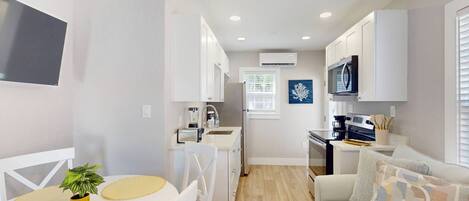 Eine kleine Küche mit weißen Schränken, einem schwarzen Herd und einem Fenster mit Jalousien.