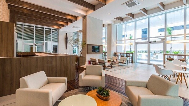 Eine moderne Lobby mit einer Rezeption, gemütlichen Sitzbereichen und großen Fenstern mit Blick ins Freie.