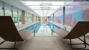 Ein Hallenbad mit zwei Liegestühlen, freier Poolblick und ein Korallen-Wandgemälde an der rechten Wand.