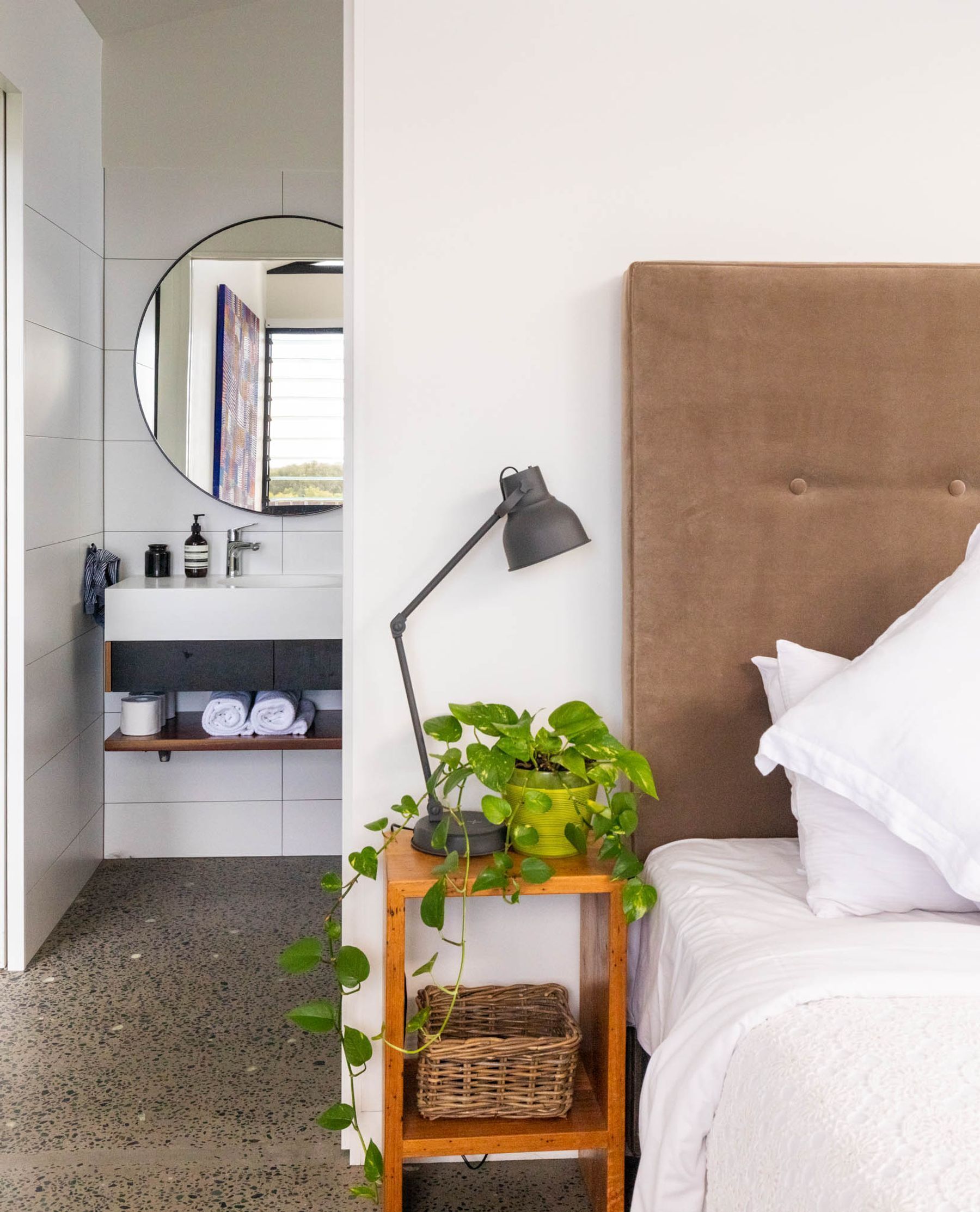 Une chambre à coucher avec un lit, une table de chevet avec une lampe, une plante en pot et un miroir.
