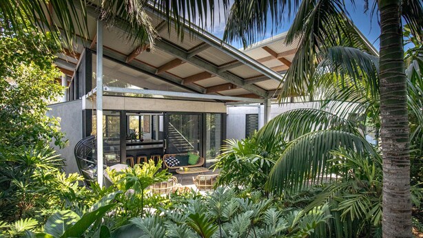 A modern house with a covered patio, outdoor furniture, and lush tropical plants.