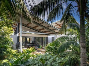 Uma casa moderna com um alpendre coberto, móveis de exterior e plantas tropicais exuberantes.