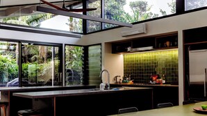 A modern kitchen with a large island, a dining area, and a view of greenery outside.