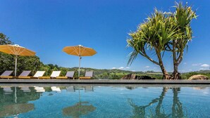 Une piscine aux eaux limpides où se reflètent les environs, avec des chaises longues et des parasols.