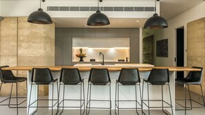 Une cuisine moderne dotée d’un îlot central, de tabourets de bar, de luminaires suspendus et d’un revêtement mural décoratif.